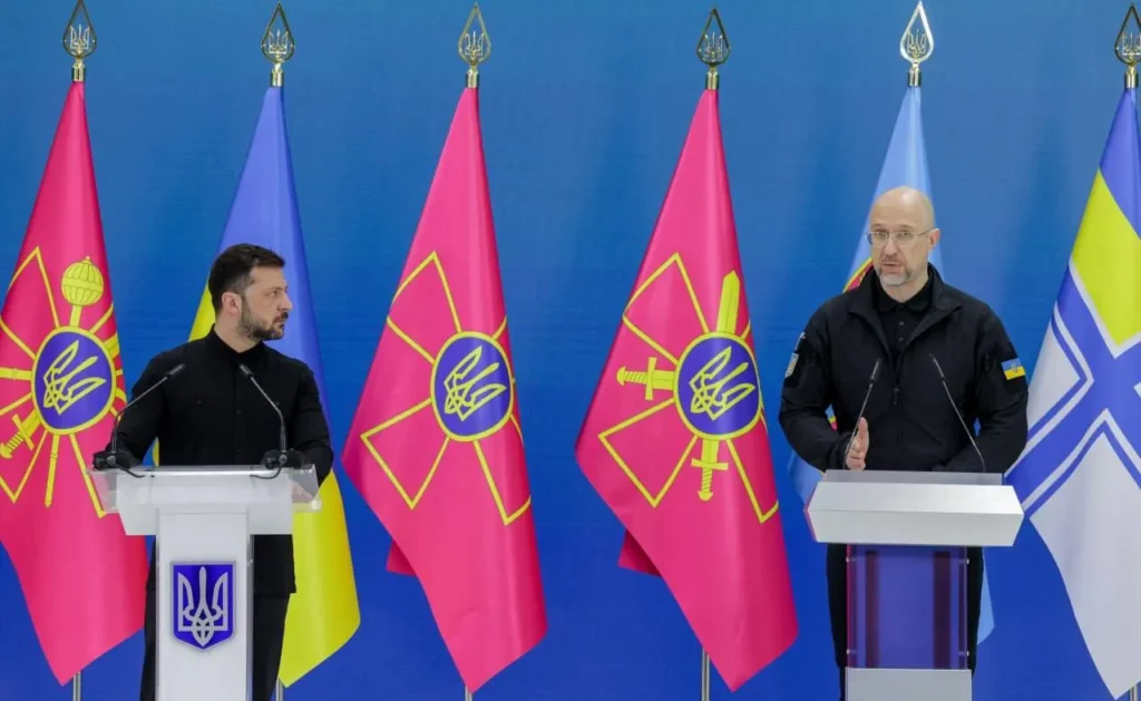 Володимир Зеленський та Денис Шмигаль за трибунами на фоні прапорів