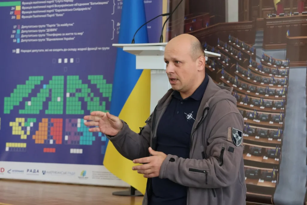 Чоловік в куртці виступає на фоні фото Верховної Ради